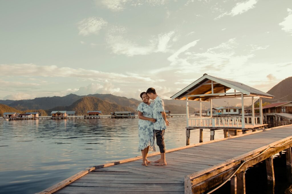 Couple relaxing on the bridge of a traditional water bungalow homestay on Kri Island, Raja Ampat.